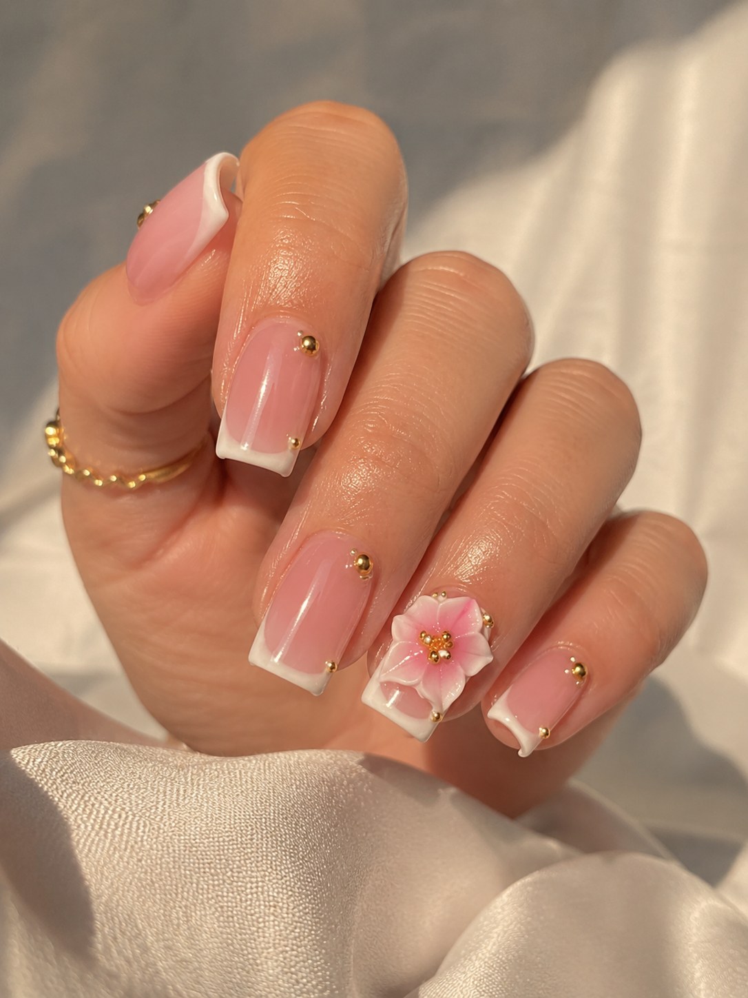 Short pink coffin nails with white French tips, gold beads, and a floral accent