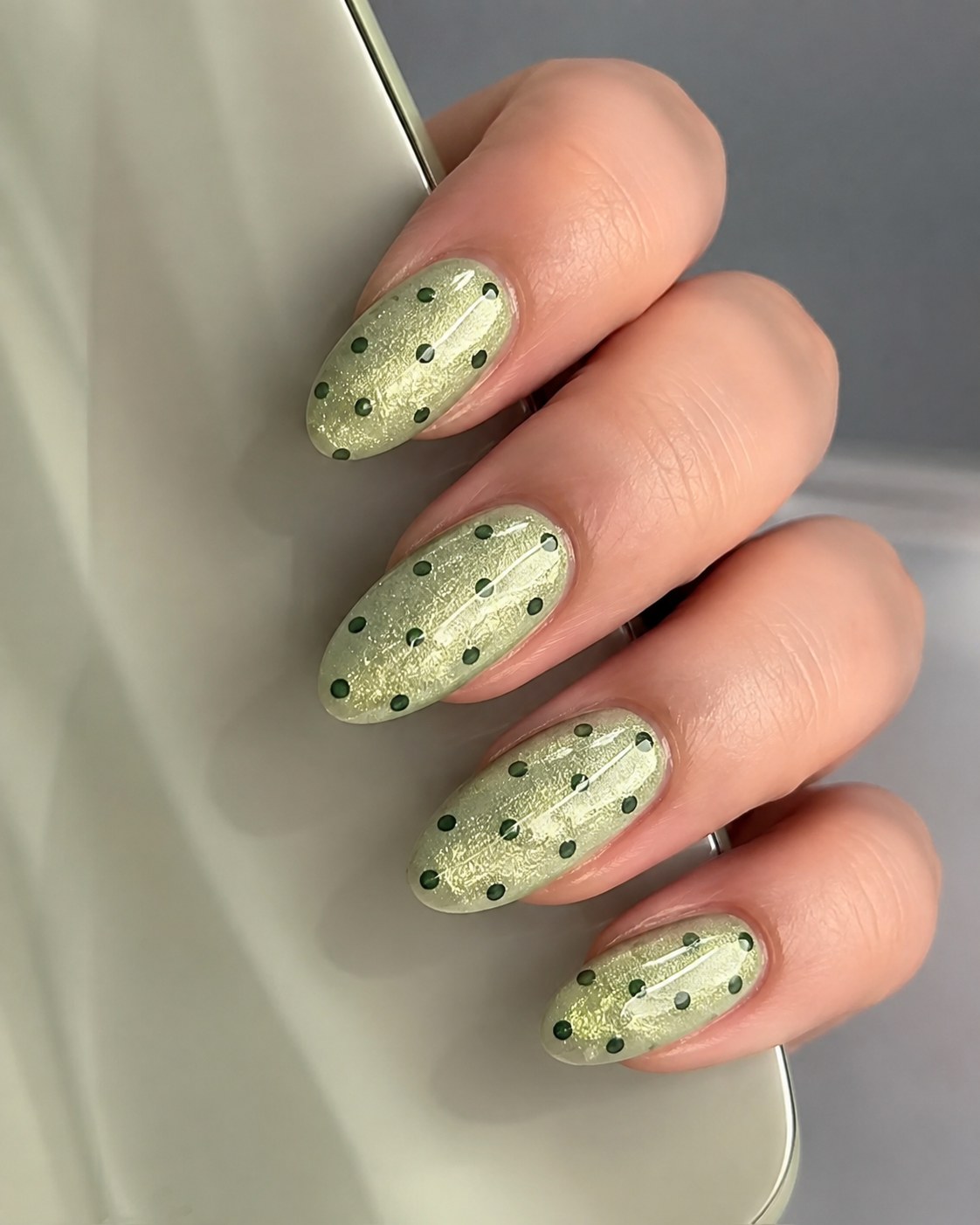 Sage green shimmer polka dot nail art with dark green dots on almond nails